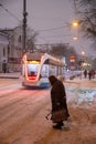 Moscow, Russia - December 7, 2022: An elderly woman crosses the road. Tram rides through the winter snowy city