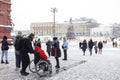 A woman carries a man in a red jacket with a disability in a wheelchair