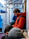 Moscow, Russia - February 8, 2020: Man rides in subway car and reads a magazine. Guy with glasses and orange jacket is standing at