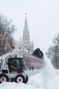 A small loader excavator bobcat removes snow from the sidewalk near the Kremlin walls during a heavy snowfall