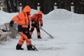 Workers in orange unform cleaning pavement from snow using shovels