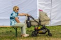 Grandmother sitting on the bench in the park and shaking the stroller with sleeping baby