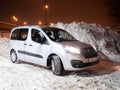 Silver car minivan Opel Combo Life against the backdrop of huge snow piles.