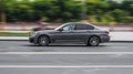 BMW 530d Sedan G30 post-facelift driving on the city street, side view. Gray car in fast motion on the highway, side view