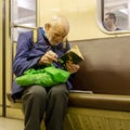 Elderly, poor, lonely man in broken glasses enthusiastically reading a tattered book