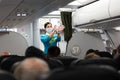 Stewardess of S7 airlines in facial mask and gloves showing emergency exit during safety instruction