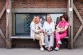Three middle-aged women sitting and talking on a bench next to a brick wall.