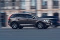 Volvo XC60 SUV in motion. Brown crossover is fast driving on city street. Side view of car moving on urban road