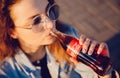 Moscow, Russia - June 27, 2019: Beautiful young woman happy drinking Coca Cola glass bottle soda in hand, sunset