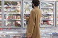 Moscow, Russia, 07/17/2020: A man in the frozen food section of a large supermarket. Young brunette with a beard in a beige coat.