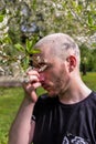 A man rubbing his nose suffering from the seasonal pollen allergy attack standing next to the flowering tree in the spring park. Royalty Free Stock Photo