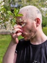 A man rubbing his nose suffering from the seasonal pollen allergy attack standing next to the flowering tree in the spring park. Royalty Free Stock Photo