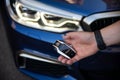 Moscow, Russia - 23 March 2019, closeup view on mans hand holding remote control key from blue bmw m550i in front of headlights.