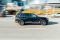 Side view rolling shot with black car in motion. BMW X7 moving along the street in city with blurred background