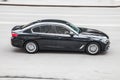 BMW 5 series G30 on the road in motion. Fast speed drive on city road. Side view of moving black car on the street