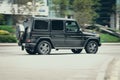 Mercedes G500 driving along the street, side view. Black premium crossover SUV in motion