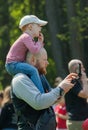Man with kid on a shoulders look at mobile phone