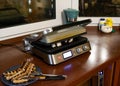 Moscow, Russia, November 2020: Working electric grill on the kitchen table. Next to it is a plate of grilled sausages