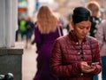 Moscow, Russia - October 19, 2019: Dark-skinned brunette Asian woman in a purple jacket holds a smartphone in her hand and walks