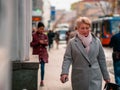 Moscow, Russia - October 19, 2019: Elderly blonde woman in coat holds  smartphone in her hand and walks along the street. The Royalty Free Stock Photo