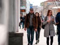 Group of people walks in a crowd of people dressed in demi-season clothes along the street. Warm autumn sunny day. City life. Side