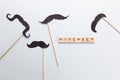 Moscow, Russia - October 07, 2019: Inscription Movember, accessories in form of black moustaches on sticks on grey background.