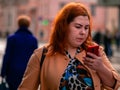 Moscow, Russia - October 19, 2019: Red-haired young plump woman holds a smartphone in her hand and walks along the street. People Royalty Free Stock Photo