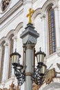 Moscow, Russia - October 03, 2019: Stone pillar with lanterns and golden cross on top against wall of Cathedral of Christ the