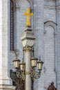 Moscow, Russia - October 03, 2019: Stone pillar with lanterns and golden cross on top against wall of Cathedral of Christ the