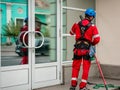Cleaner with mop prepares to wash windows in historical architecture building. Worker in branded red overalls, helmet and special Royalty Free Stock Photo