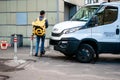 Courier of food delivery service in a branded uniform with a yellow Yandex-Eda backpack next to truck car. Thermal bag with symbol