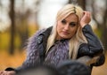 A young attractive woman wearing fur black jacket holding book sitting on the bench in falling park. Royalty Free Stock Photo