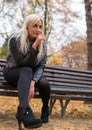 A young attractive woman wearing fur black jacket holding book sitting on the bench in falling park. Royalty Free Stock Photo