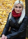 A young attractive woman wearing fur black jacket holding book sitting by the tree. Walking around autumn park. Royalty Free Stock Photo