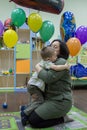 Young woman and her little son sitting on the chair on background of colorful balloons.