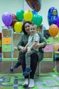 Young woman and her little son sitting on the chair on background of colorful balloons.