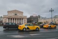 a stream of cars and yellow taxis travels fast against the backdrop of the Bolshoi Theater in Moscow