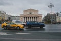 a stream of cars and yellow taxis travels fast against the backdrop of the Bolshoi Theater in Moscow