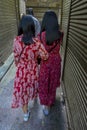 Moslem People of Egypt go shopping at Luxor Souq - two women wear bright red dresses from behind