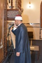 A mosque Imam preacher muezzin in front of the microphone reciting Adhan Azan or calling loudly for the prayer