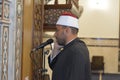 A mosque Imam preacher muezzin in front of the microphone reciting Adhan Azan or calling loudly for the prayer