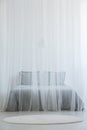 Mosquito net bed with grey bedding standing in white room interior with round rug on the floor Royalty Free Stock Photo