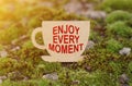On the moss in the rays of the sun, a cup with the inscription - ENJOY EVERY MOMENT Royalty Free Stock Photo
