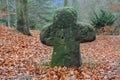 a mossy green old tombstone cross in the midst of dry leaves in autumn forest Royalty Free Stock Photo