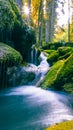 Mossy rocks and waterfall illuminated by sunlight streaming through dense autumn forest Royalty Free Stock Photo