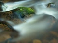 Mossy stone in blurred blue waves of mountain stream. Cold water is running and turning between boulders and bubbles create tr Royalty Free Stock Photo