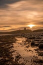 The most beautiful sunrise at Dunstanburgh Castle with the famous slippery black boulders in Northumberland, as the sky erupted wi Royalty Free Stock Photo