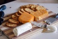 Dairy products - three types of cheese, cheese knife and salted crackers on a wooden curtting board