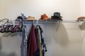 A mostly empty walk in messy closet with some hanging clothes and hats