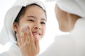 Mother adding treatment cream on the cheek to young and cute Asian girl with spa dress and head covered with a white towel Royalty Free Stock Photo